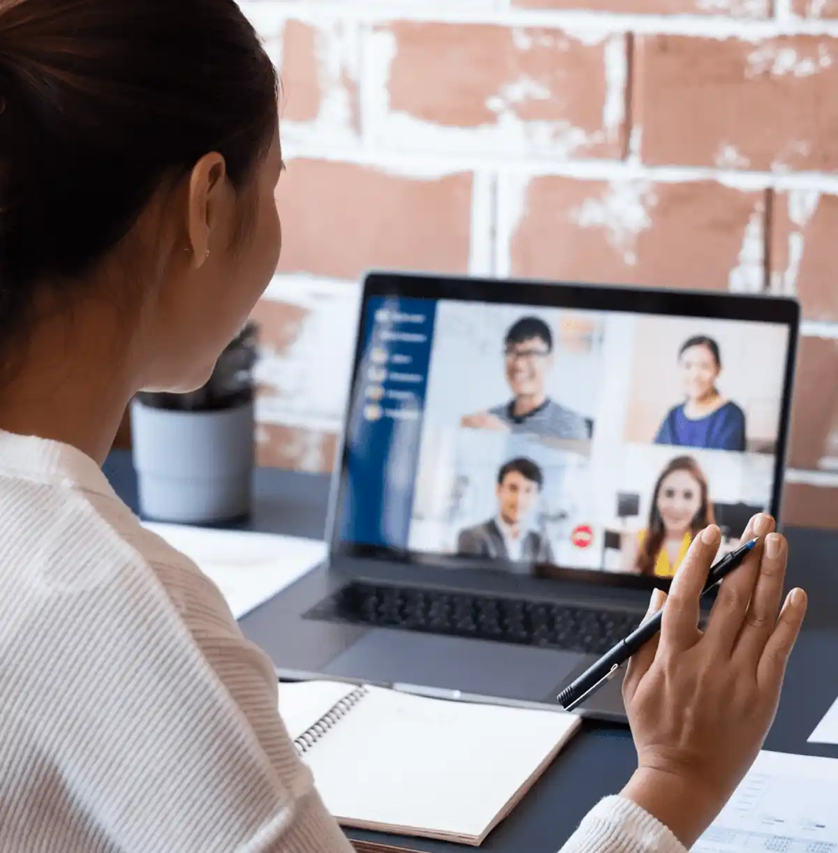 Woman holding a pen while joining a video conference with four participants visible on her laptop screen