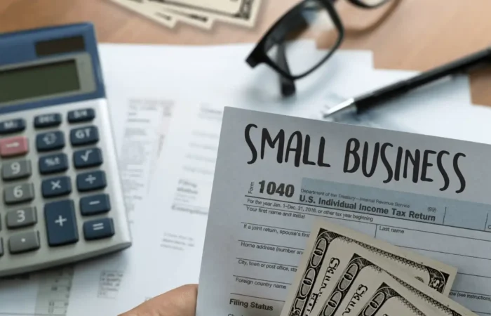 Person holding small business tax form with cash, calculator, and paperwork on a desk